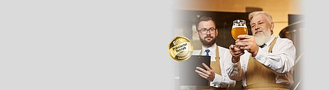 Bierbrauer zeigt einem anderen Bierbrauer ein Glas mit Bier.