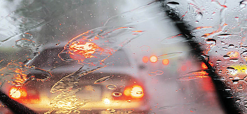 Blick durch regennasse Windschutzscheibe auf vorausfahrendes Auto mit Bremsleuchten