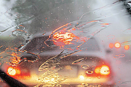 Blick durch regennasse Windschutzscheibe auf vorausfahrendes Auto mit Bremsleuchten