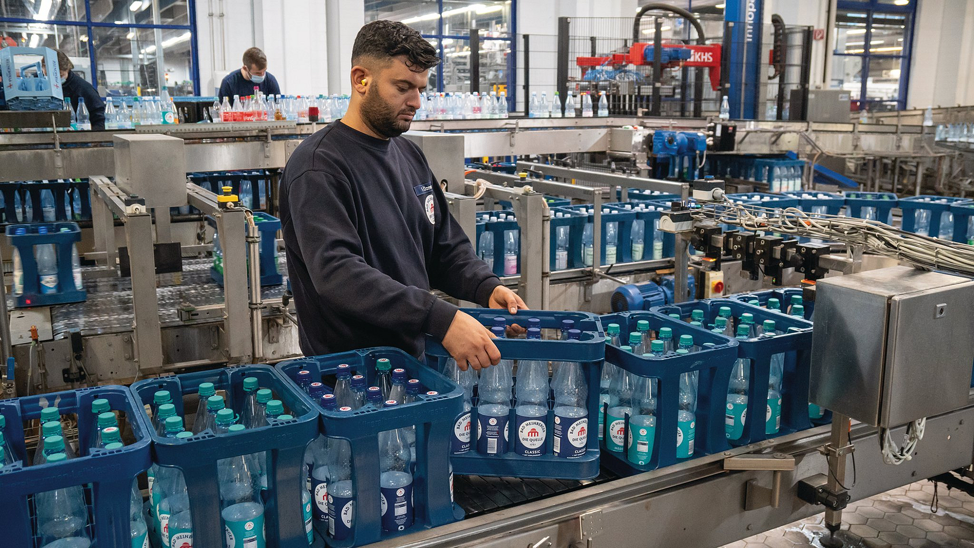 Ein junger Mitarbeiter setzt einen Getränkekasten auf ein Fließband.