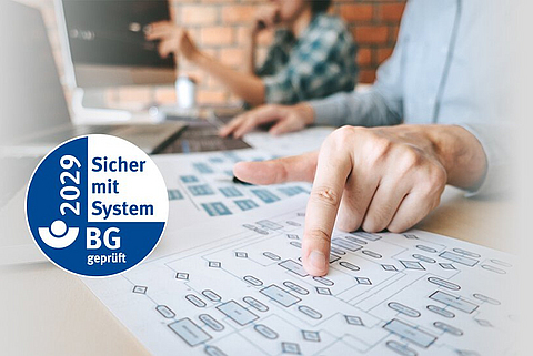 Ein Mann sitzt am Schreibtisch und zeigt auf ein Blatt Papier mit einem Diagramm, daneben das AMS-Gütesiegel.