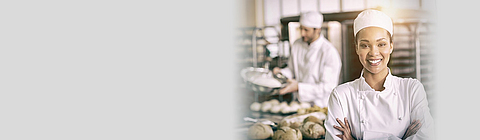 Bäckerin steht in der Bäckerei und lacht in die Kamera.
