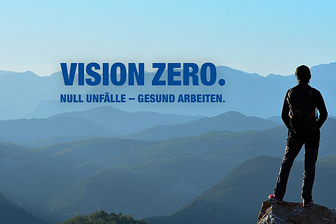 Eine Person steht auf einem Berg und schaut in die Weite. Im Berg ist das Logo für "VISION ZERO".