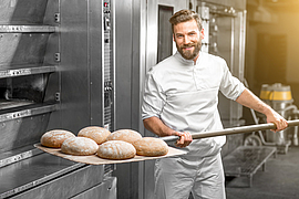 Bäcker holt fertig gebackenes Brot aus dem Ofen