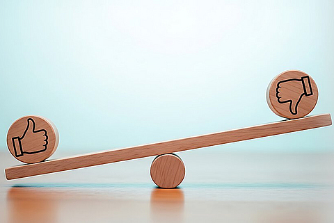 Eine hölzerne Wippe, die ein Daumen-hoch- und ein Daumen-runter-Symbol im Gleichgewicht hält