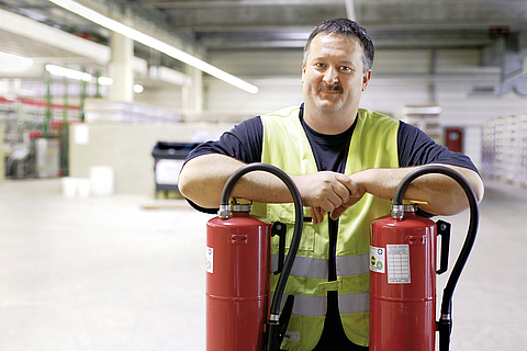 Sicherheitsfachkraft wird mit zwei Feuerlöscher in einer Lagerhalle fotografiert