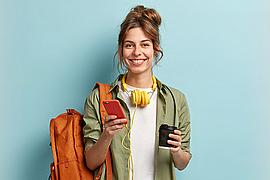 Frau mit Rucksack hält Smartphone in der einen und Kaffeebecher in der anderen Hand