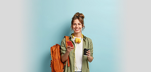 Frau mit Rucksack hält Smartphone in der einen und Kaffeebecher in der anderen Hand