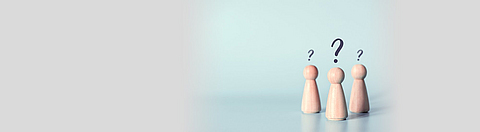 Drei Spielfiguren aus Holz Mit Fragezeichen über dem Kopf auf hellblauen Hintergrund.