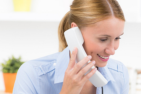 Eine freundliche junge Damen hält einen Telefonhörer in der Hand