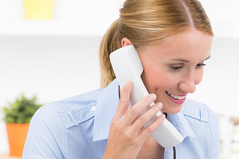 Eine freundliche junge Damen hält einen Telefonhörer in der Hand