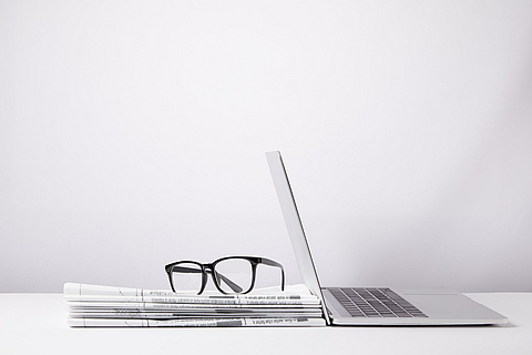 Ein Stapel Zeitungen mit Lesebrille und Laptop