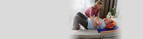 Eine Frau hilft einem Mann sich richtig auf ein Bett zu legen.