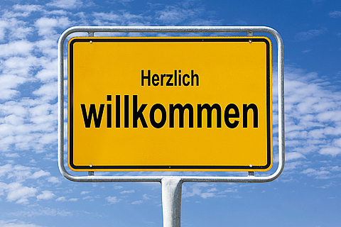 Ein Ortsschild vor blauem Himmel auf dem Herzlich willkommen steht