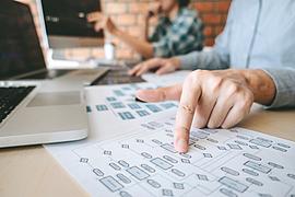 Ein Mann sitzt vor einem Schreibtisch und zeigt auf ein Blatt Papier mit einem Diagramm.