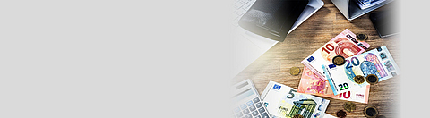 Geldscheine und Geldmünzen liegen durcheinander auf einem Tisch.