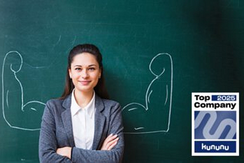 Eine junge Frau steht vor einer Tafel, auf der Tafel sind Arme mit großen Muskeln aufgemalt.