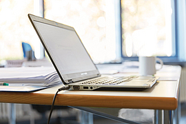 Ein Laptop steht auf einem Tisch, im Hintergrund eine Tasse.