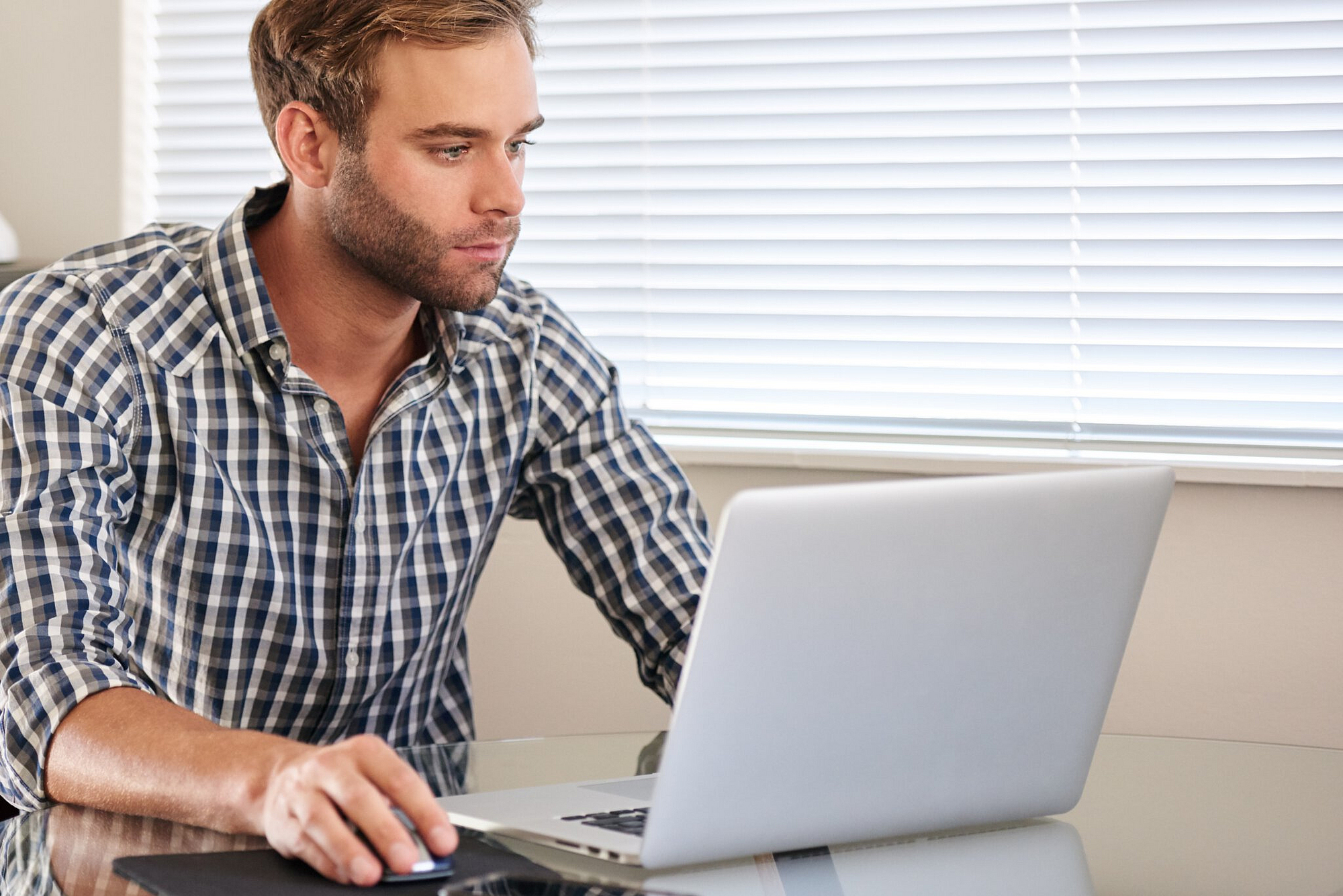 Junger weißer Mann, der damit beschäftigt ist, die Maus zu halten, während er mit seinem modernen Notebook von zu Hause aus online arbeitet