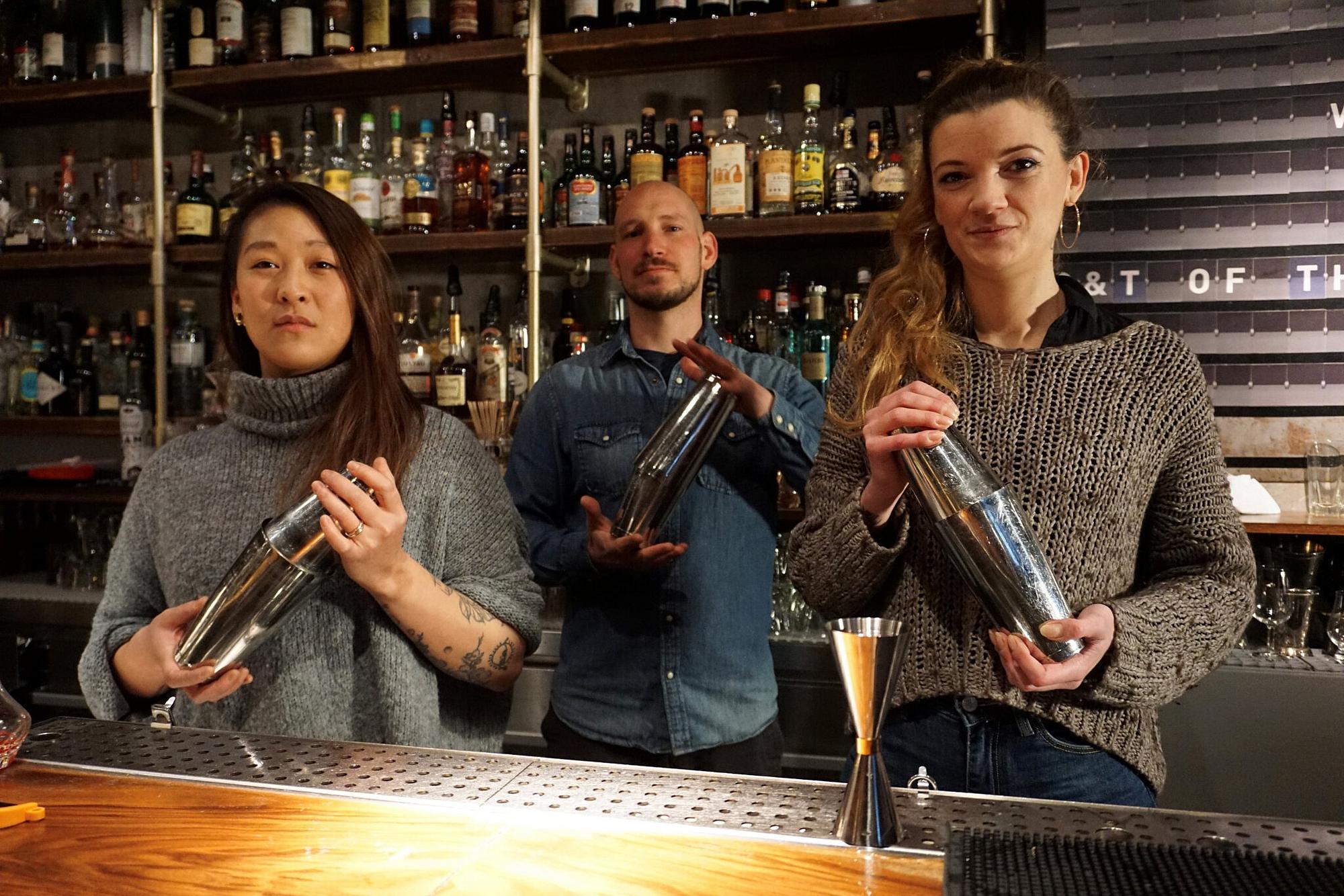 Drei Mitarbeitende stehen hinter einer Bar und mixen Getränke.