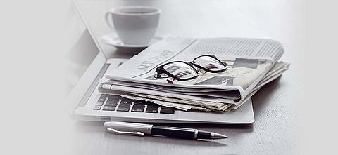 Auf einem Laptop liegt eine Zeitung und eine Brille.