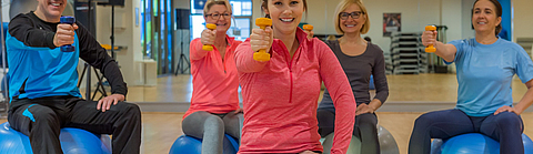 Gruppe trainiert mit Hanteln auf dem Gymnastikball
