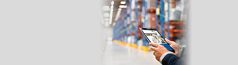 Ein Tablet mit einer ASI der BGN wird in Hand gehalten, im Hintergrund eine Lagerhalle.