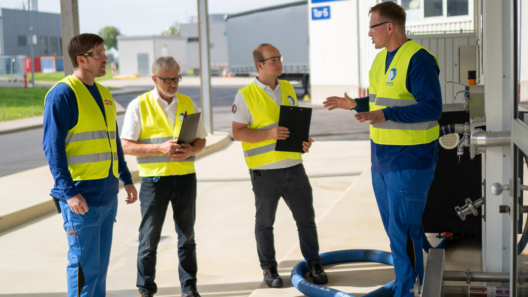 Vier Mitarbeiter von Milupa stehen mit Klemmbrettern und Warnwesten vor dem Eingang eines Gebäudes und besprechen sich.