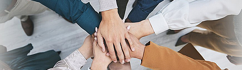 Viele Menschen strecken ihre Arme aus und legen in der Mitte ihre Hände übereinander als Zeichen der Verbundenheit.