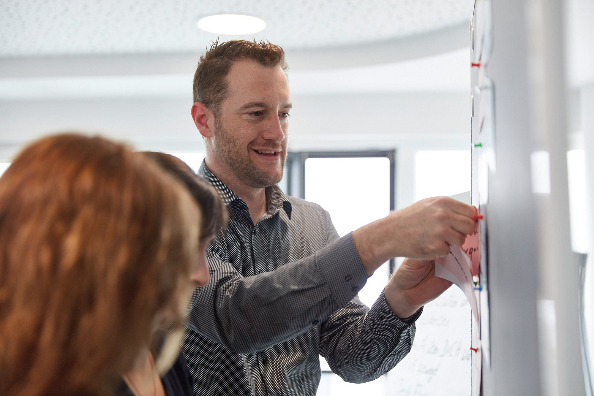 Ein Mitarbeiter macht bei einer Besprechung einen Zettel an eine Pinnwand.
