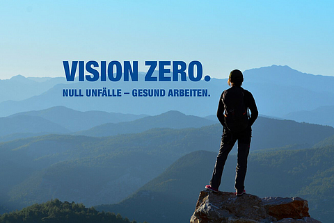 Eine Person steht auf einem Berggipfel und schaut in die Ferne. Daneben steht "Vision Zero. Null Unfälle - gesund arbeiten."