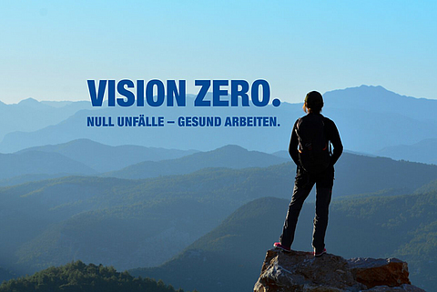 Eine Person steht auf einem Berggipfel und schaut in die Ferne. Daneben steht "Vision Zero. Null Unfälle - gesund arbeiten."