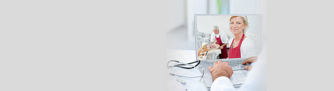 Blick über die Schulter eines Arztes auf einen Laptop, der Bildschirm zeigt zwei Angestellte einer Metzgerei.