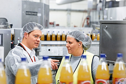 Eine Fachkraft für Arbeitssicherheit unterweist eine Mitarbeiterin in der Getränkeproduktion