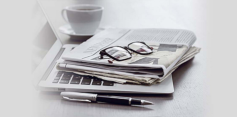Auf einem Laptop liegt eine Zeitung und eine Brille.