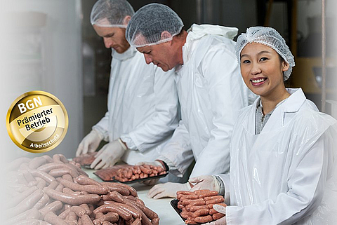 Eine Mitarbeiterin und zwei Mitarbeiter eines Fleischereibetriebs tragen Schutzkleidung und packen Wurstwaren ab.