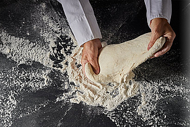 Auf einer schwarzen Unterlage wird ein Teigling geknetet.