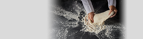 Auf einer schwarzen Unterlage wird ein Teigling geknetet.