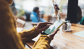 Eine Frau hält in einem Café ein Handy in der Hand und tippt etwas ein