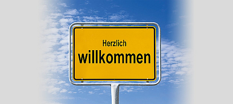 Ein Ortsschild vor blauem Himmel auf dem Herzlich Willkommen steht.