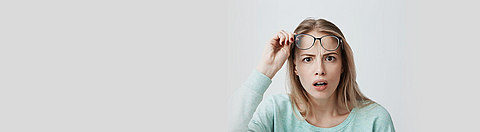 Eine Frau reißt vor Erstaunen die Augen auf und zieht ihre Brille ab.