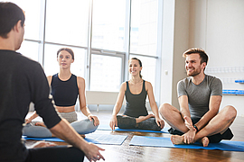 Junge Menschen, die auf Trainingsmatten sitzen und den Yogalehrer anschauen, während sie dem Vortrag im Yoga-Seminar lauschen