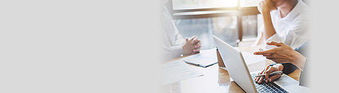 Besprechung an einem Tisch auf dem Dokumente liegen und ein Laptop