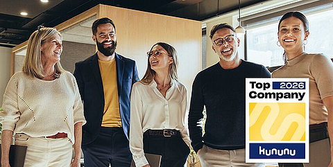 Kollegen stehen im Büro zusammen und lachen.