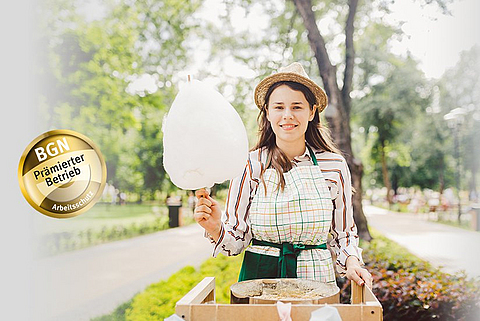 Verkäuferin hält Zuckerwatte in der Hand und lächelt in die Kamera.