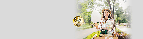 Verkäuferin hält Zuckerwatte in der Hand und lächelt in die Kamera.