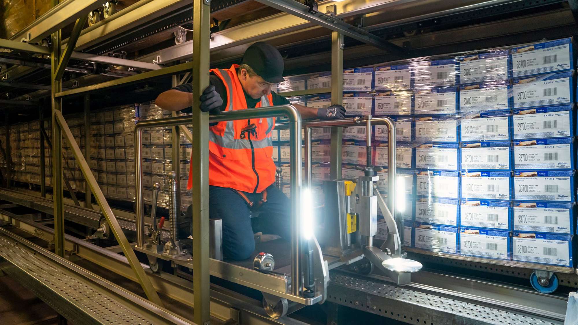 Ein Mitarbeiter kniet auf einem Gleiswagen in einem Rollpalettenlager.