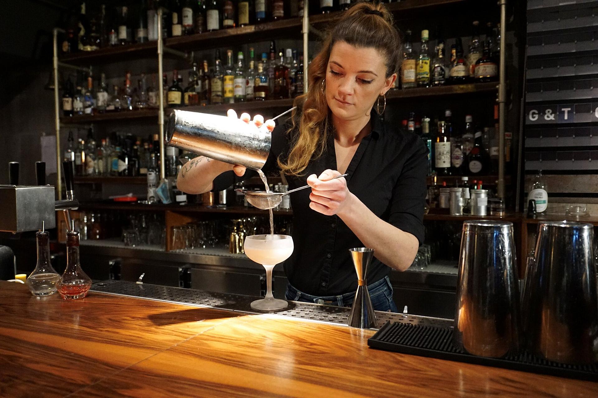 Eine Mitarbeiterin steht hinter einer Bar und mixt ein Getränk.