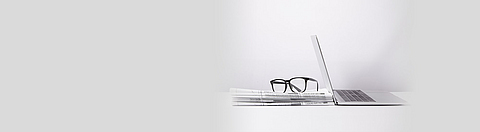 Ein Stapel Zeitungen mit Lesebrille und Laptop