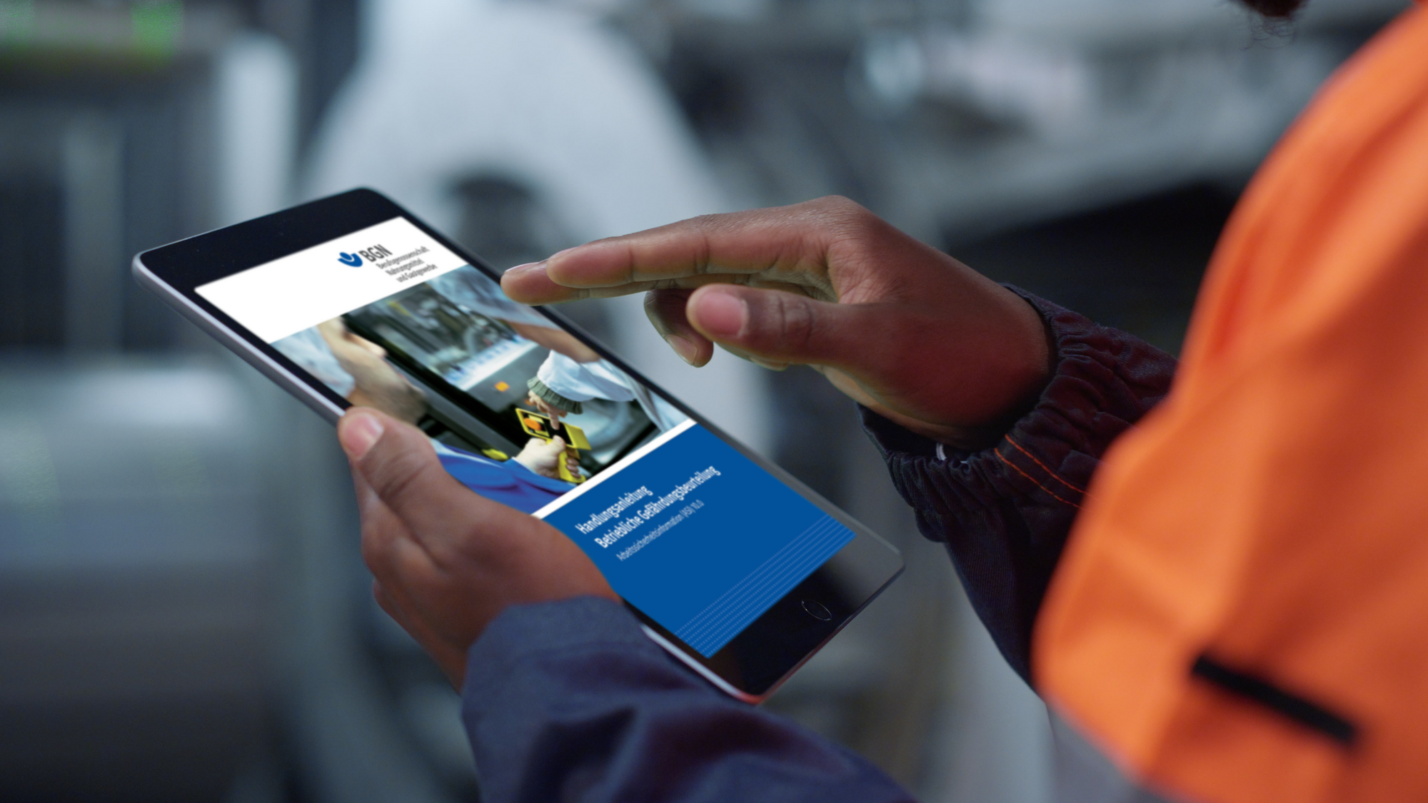  Ein Mann in Arbeitskleidung hält in einer Produktionsanlage ein Tablet in der Hand